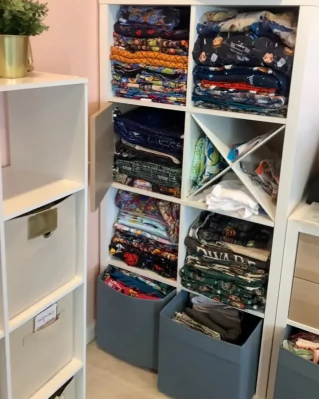 A craft room with fabric folded and shelved by colour in cube storage